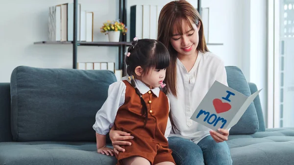 Young asia mother sitting on couch with child daughter reading fairy tales together. Child daughter reading book learning education fairy tale story bonding enjoying with mom in living room