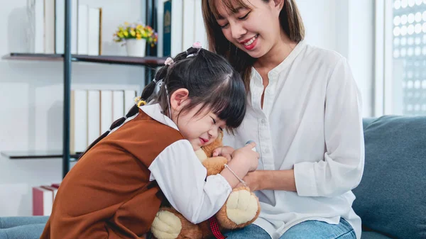 Smiling mother and daughter hugging teddy bear toy, Portrait of happy asia family mum and child together holding teddy bear in modern living room, Happy loving family asia