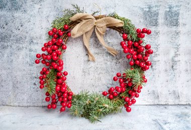 Çam ağacından Noel çelengi koni, böğürtlen ve kırmızı kurdeleli ladin dalları gri desenli arka planda 