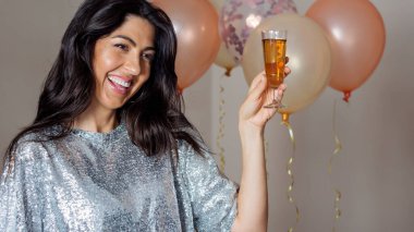 Beautiful laughing woman with shiny dress holding glass of wine on balloons background .Party time concept