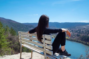 Gölün yukarısındaki bankta oturan ve cep telefonuna bakan kadın.