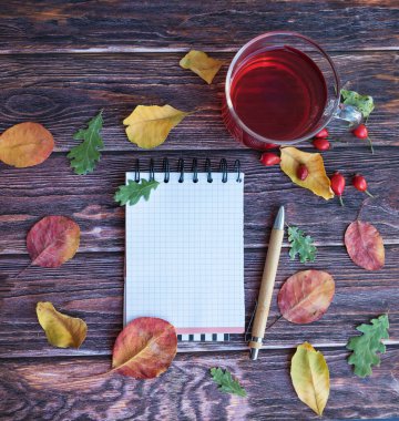 Not defteri, çay fincanı ve sonbahar yaprakları ahşap arka planda