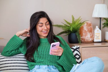 Evde oturan ve cep telefonu kullanan güzel, genç bir kadın.