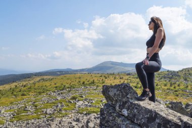 Yaz dağında kayaların üzerinde duran bir kadın.