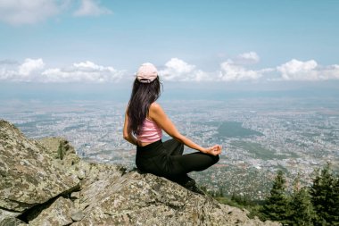 Genç Kadın Lotus pozisyonunda dağın tepesinde meditasyon yapıyor. Doğadaki Yoga Doğası. Şehrin yukarısında