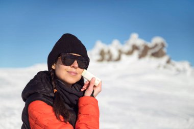 Kışın dağa güneş kremi süren genç bir kadın.