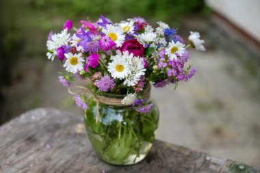 Güzel bir buket yaz çiçeğiyle ahşap bir bankta cam vazo