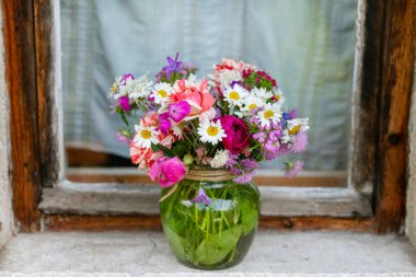 Güzel bir buket yaz çiçeğiyle ahşap bir bankta cam vazo