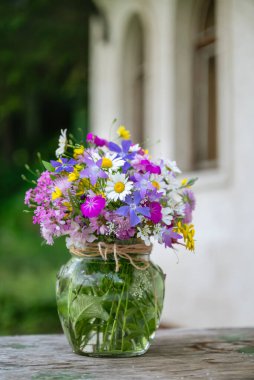 Güzel bir buket yaz çiçeğiyle ahşap bir bankta cam vazo