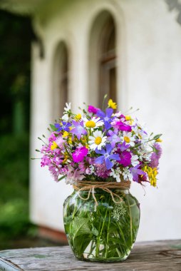 Güzel bir buket yaz çiçeğiyle ahşap bir bankta cam vazo