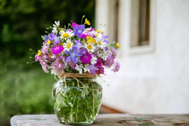 Güzel bir buket yaz çiçeğiyle ahşap bir bankta cam vazo