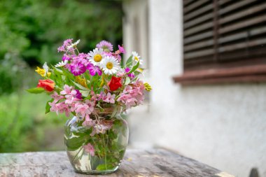 Güzel bir buket yaz çiçeğiyle ahşap bir bankta cam vazo