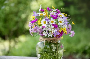 Güzel bir buket yaz çiçeğiyle ahşap bir bankta cam vazo