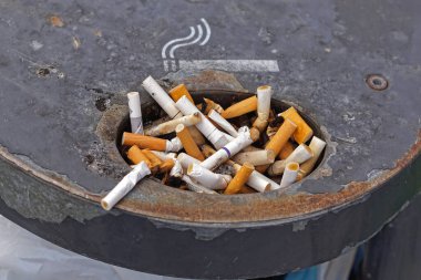 Aşırı yüklenmiş sigara izmaritleri açık hava kül tablasına atılmış.