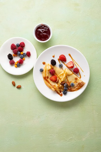 Overhead view of crepes with berries and jam food on light surface