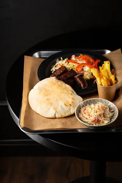 Overhead view of pita bread with meat and salad on black table