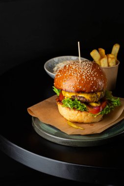 Peynirli burger ve patates siyah bir masada.