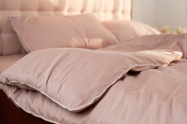 Yatağın üzerinde açık bej rengi saten yatak, yastıklar ve battaniye.