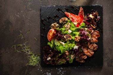 Siyah tahtada ızgara et dilimlenmiş sebze salatası.