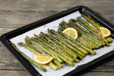 Fırınlanmış yeşil kuşkonmaz ve limonlu fırın tepsisi ve ahşap yüzeyde sert peynir.