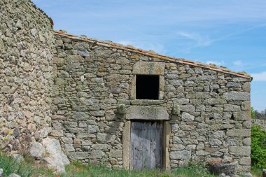 a stone house wall with open window and old wooden door
