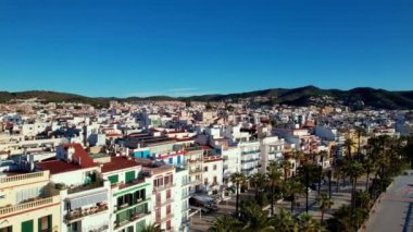 İspanya 'nın Katalonya kenti Barselona yakınlarındaki Sitges kasabasında güneşli bir günde Sant Bartomeu i Santa Tecla de Sitges kıyı köyünün panoramik manzarası. Plajlarıyla ünlüdür. Film tanıtımı. 4K video