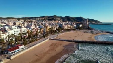 İspanya 'nın Katalonya kenti Barselona yakınlarındaki Sitges kasabasında güneşli bir günde Sant Bartomeu i Santa Tecla de Sitges adlı kıyı köyünün panoramik hava aracı görüntüsü. Plajları ve gece hayatıyla ünlüdür.