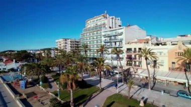 İspanya 'nın Barselona eyaletinin Akdeniz kasabası Sitges' de güneşli bir günde deniz kıyısındaki Sant Bartomeu i Santa Tecla de Sitges köyünün panoramik manzarası. Film tanıtımı. 4K