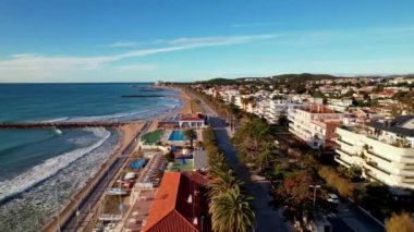 İHA, sahil boyunca Sitges 'deki palmiye ağaçlarıyla çevrili güzel plajlarda uçuyor. Akdeniz manzaralı plaj ve oteller. Yumuşak deniz dalgaları sessizce kıyıya vurur. Film tanıtımı. 4K video