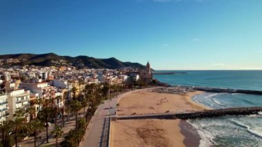 İspanya 'nın Katalonya kenti Barselona yakınlarındaki Sitges kasabasında güneşli bir günde Sant Bartomeu i Santa Tecla de Sitges kıyı köyünün panoramik manzarası. Plajlarıyla ünlüdür. Film tanıtımı. 4K video