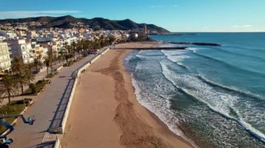 İspanya 'nın Katalonya kenti Barselona yakınlarındaki Sitges kasabasında güneşli bir günde Sant Bartomeu i Santa Tecla de Sitges kıyı köyünün panoramik manzarası. Plajlarıyla ünlüdür. Film tanıtımı. 4K video