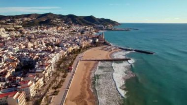 İspanya 'nın Barselona eyaletinin Akdeniz kasabası Sitges' de güneşli bir günde deniz kıyısındaki Sant Bartomeu i Santa Tecla de Sitges köyünün panoramik manzarası. Film tanıtımı. 4K