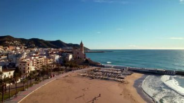 İspanya 'nın Katalonya kenti Barselona yakınlarındaki Sitges kasabasında güneşli bir günde Sant Bartomeu i Santa Tecla de Sitges adlı kıyı köyünün panoramik hava aracı görüntüsü. Plajları ve gece hayatıyla ünlüdür.