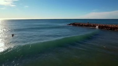 Deniz manzaralı, deniz manzaralı, deniz dalgaları kıyıya vuruyor. Sörfçü sporcu dalgalar arasında yüzer, mükemmel sörf noktasına ulaşmak için kürek çeker. Yaz tatili kavramı. 4K video