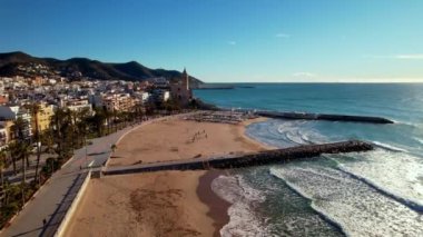 İspanya 'nın Katalonya kenti Barselona yakınlarındaki Sitges kasabasında güneşli bir günde Sant Bartomeu i Santa Tecla de Sitges adlı kıyı köyünün panoramik hava aracı görüntüsü. Plajları ve gece hayatıyla ünlüdür.