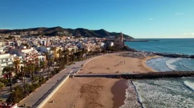 İspanya 'nın Katalonya kenti Barselona yakınlarındaki Sitges kasabasında güneşli bir günde Sant Bartomeu i Santa Tecla de Sitges kıyı köyünün panoramik manzarası. Plajlarıyla ünlüdür. Film tanıtımı. 4K video