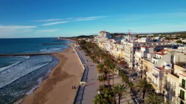 İHA, sahil boyunca Sitges 'deki palmiye ağaçlarıyla çevrili güzel plajlarda uçuyor. Akdeniz manzaralı plaj ve oteller. Yumuşak deniz dalgaları sessizce kıyıya vurur. Film tanıtımı. 4K video