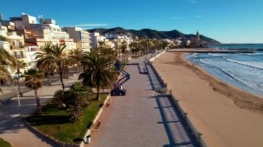 İHA, sahil boyunca Sitges 'deki palmiye ağaçlarıyla çevrili güzel plajlarda uçuyor. Akdeniz manzaralı plaj ve oteller. Yumuşak deniz dalgaları sessizce kıyıya vurur. Film tanıtımı. 4K video