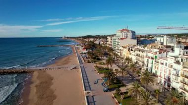 İHA, sahil boyunca Sitges 'deki palmiye ağaçlarıyla çevrili güzel plajlarda uçuyor. Akdeniz manzaralı plaj ve oteller. Yumuşak deniz dalgaları sessizce kıyıya vurur. Film tanıtımı. 4K video