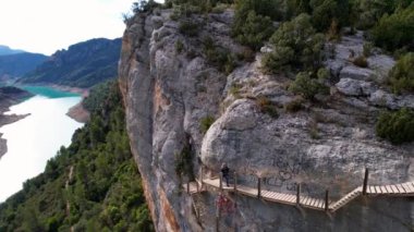 İspanya, Pireneler 'deki Congost de Montrebei vadisindeki yürüyüş yolunun bir parçası olarak kayalıklardaki ahşap merdivenlerin panoramik ve etkileyici hava manzarası. Üst kata çıkan bir grup insan. 4K