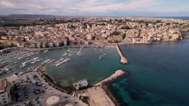 Syracuse, İtalya 'da insansız hava aracı keşiflerine çıkın, şehirlerin ikonik mirasını ve cennet kıyı şeritlerini sergileyin. Parlak yatlar, güneşli denizde sürükleniyor. Lüks ve sükunetin büyüleyici bir sahnesini oluşturuyor.