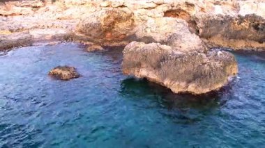 Sicilya 'lı Ognina Spiaggia di Punta Asparano' nun nefes kesici insansız hava aracı görüntüleri. Göz kamaştırıcı sahil uçurumlarının üzerinde süzülür, doğal kayalık kemer, parıldayan Akdeniz kıyıları. Seyahat ve doğa tutkunları için