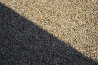 Çapraz çapraz gölgelerle örtülmüş küçük, çok renkli çakıl taşlarının yakın plan çekimi sanatsal ve tasarım amaçlarına uygun dinamik ve dokulu bir arkaplan oluşturur.