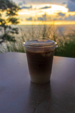 Gün batımında sahilde bir bardak kahve ya da kahve.