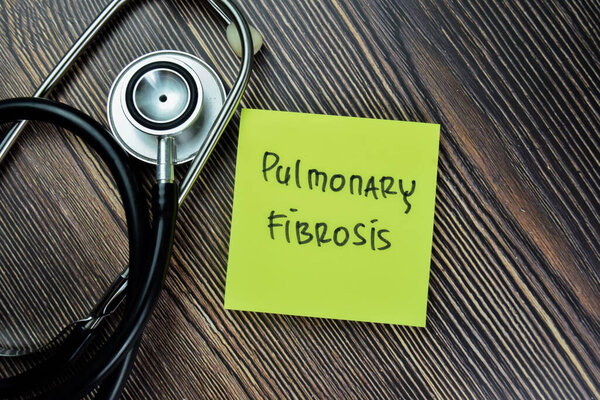 Concept of Pulmonary Fibrosis write on sticky notes with stethoscope isolated on Wooden Table.