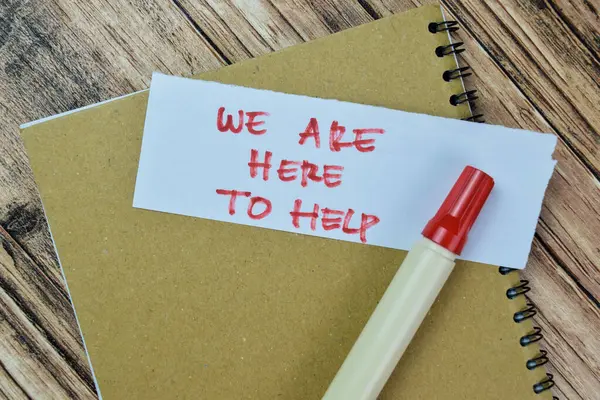 Concept of We Are Here To Help write on sticky notes isolated on Wooden Table.