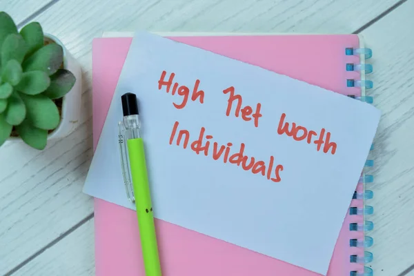 Concept of High Net Worth Individuals write on sticky notes isolated on Wooden Table.