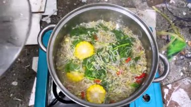 Sayur bening bayam, ıspanak temizleme sebzesi pişiren genç bir adam. Endonezya yemeği ıspanak, mısırlı ıspanak çorbası