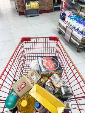 Yiyecek ve içeceklerle dolu alışveriş arabası ve arka planda süpermarket rafları, market alışveriş konsepti. Bekasi, Endonezya, 22 Nisan 2024