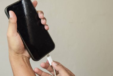 Cep telefonları şarj oluyor. Adam akıllı telefondan şarj aletini fişe takıyor.